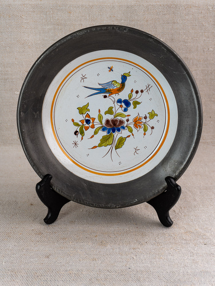 French faience wall plate with hand-painted Moustiers-style bird and floral motifs, pewter rim, on stand.