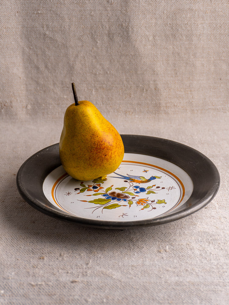 French Faience wall plate, Moustiers style, bird and floral motifs, pewter rim, beige fabric background.