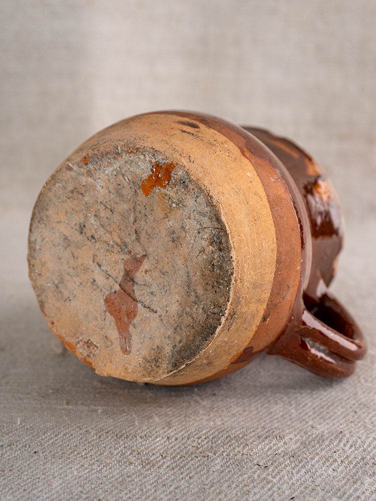 19th century French Pichet, glazed earthenware mug with rustic half-dipped design on light textured fabric.