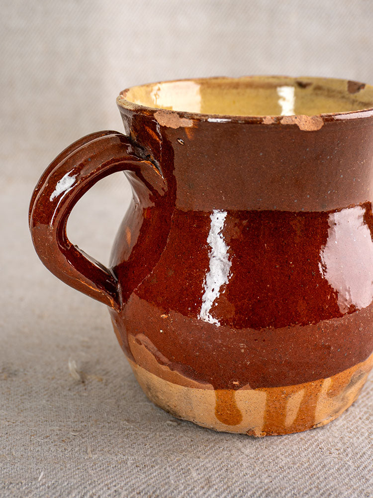 19th century French glazed earthenware pichet with rustic half-dipped finish on textured beige fabric.