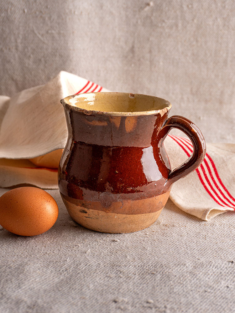 19th century French glazed earthenware pichet with half-dipped finish on textured gray fabric with rustic linen and egg.