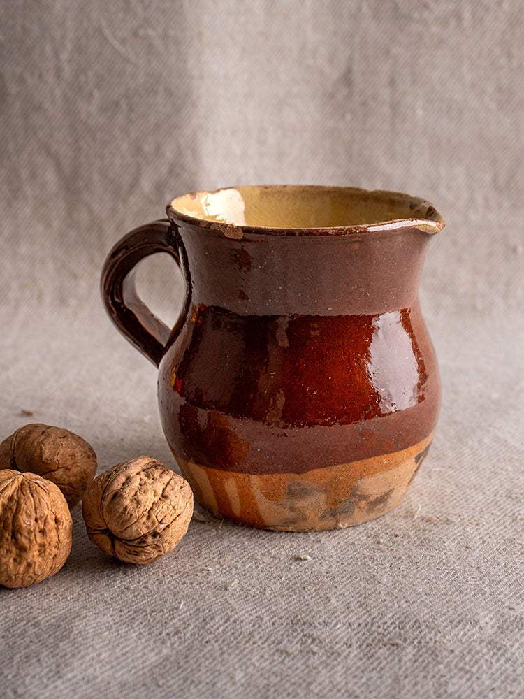19th-century French glazed earthenware pichet with rustic half-dipped design and handle, on gray fabric with walnuts.