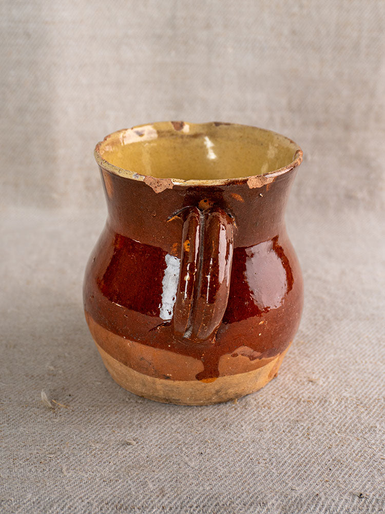 19th century French earthenware pichet with chipped rim, half-glazed finish, on textured beige fabric.