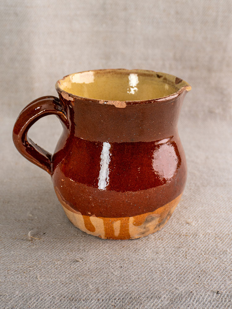 19th century French earthenware pichet with single handle and unglazed base on textured light fabric.