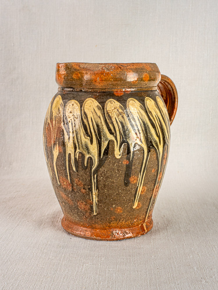 Antique French Pichet Jaspé ceramic jug with brown glaze and cream drip, Savoie, on fabric background.