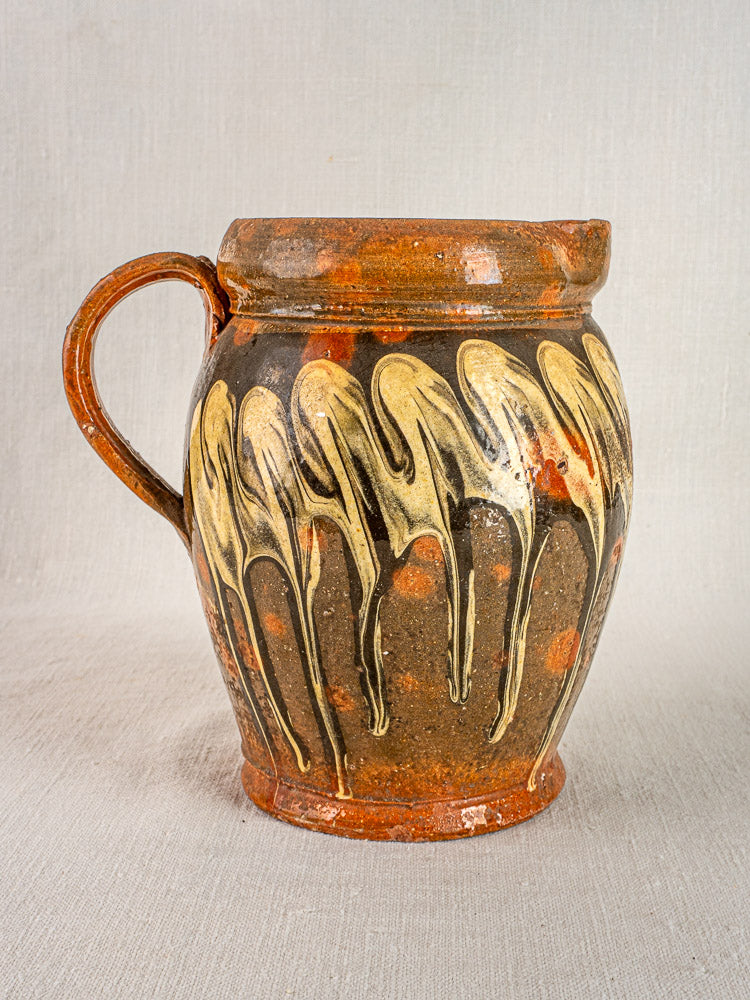 Antique French Pichet Jaspé, late 19th century Savoie pottery jug with yellowish drip glaze, on neutral fabric background.