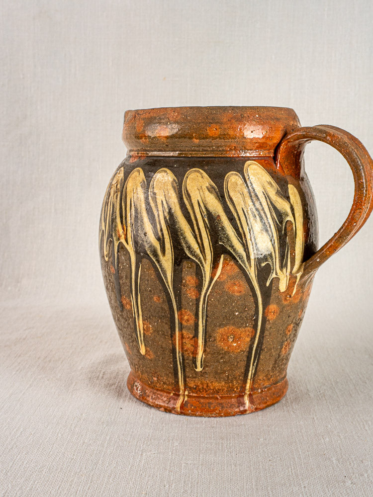 Antique French Savoie brown ceramic pichet jaspé with yellow glaze drips and orange spots on fabric background.