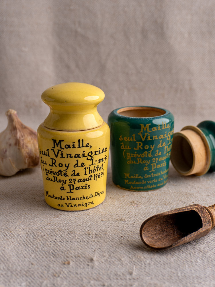 Pair of vintage French Maille mustard pots, teal and yellow, with wooden lids on beige fabric.