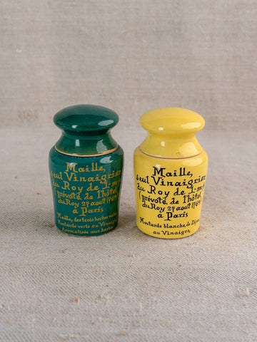 Pair of vintage French Maille mustard pots, teal and yellow, with French lettering and round lids on beige fabric.