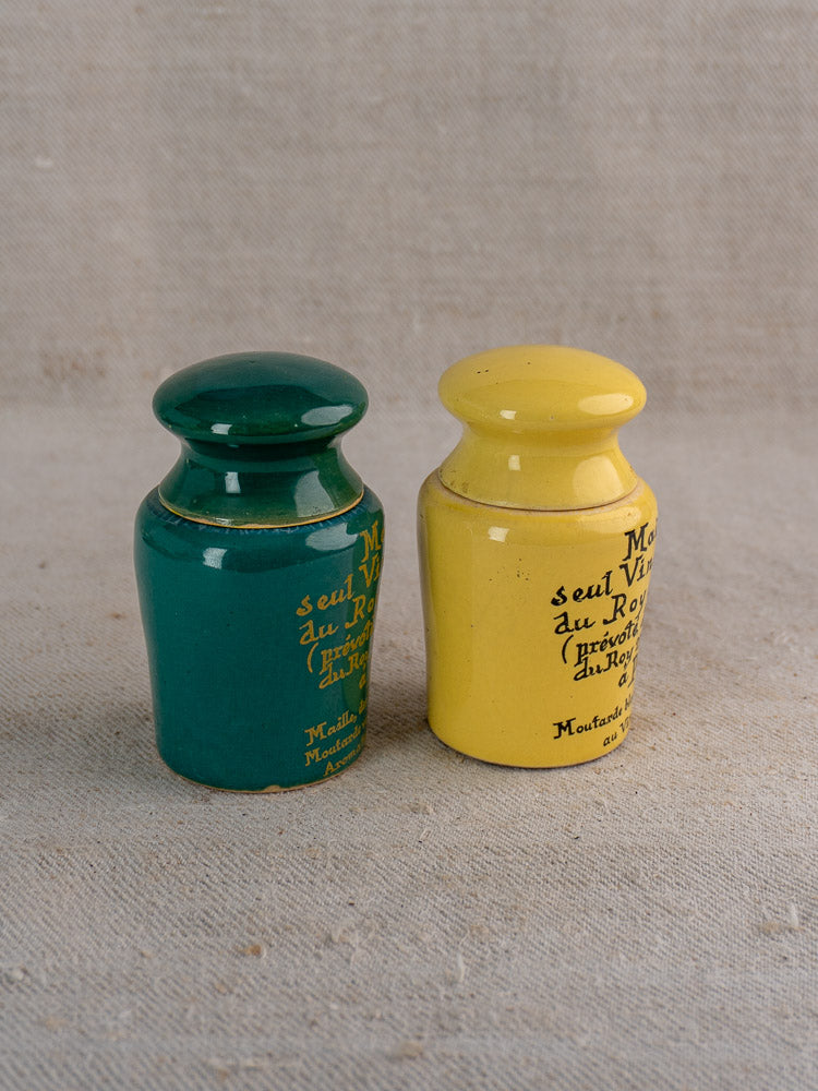 Vintage French Maille mustard pots in teal and yellow with classic lettering on fabric background.