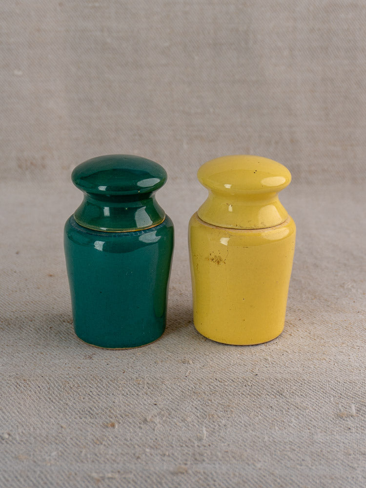 Pair of vintage French Maille mustard pots, teal and yellow, on textured beige fabric.