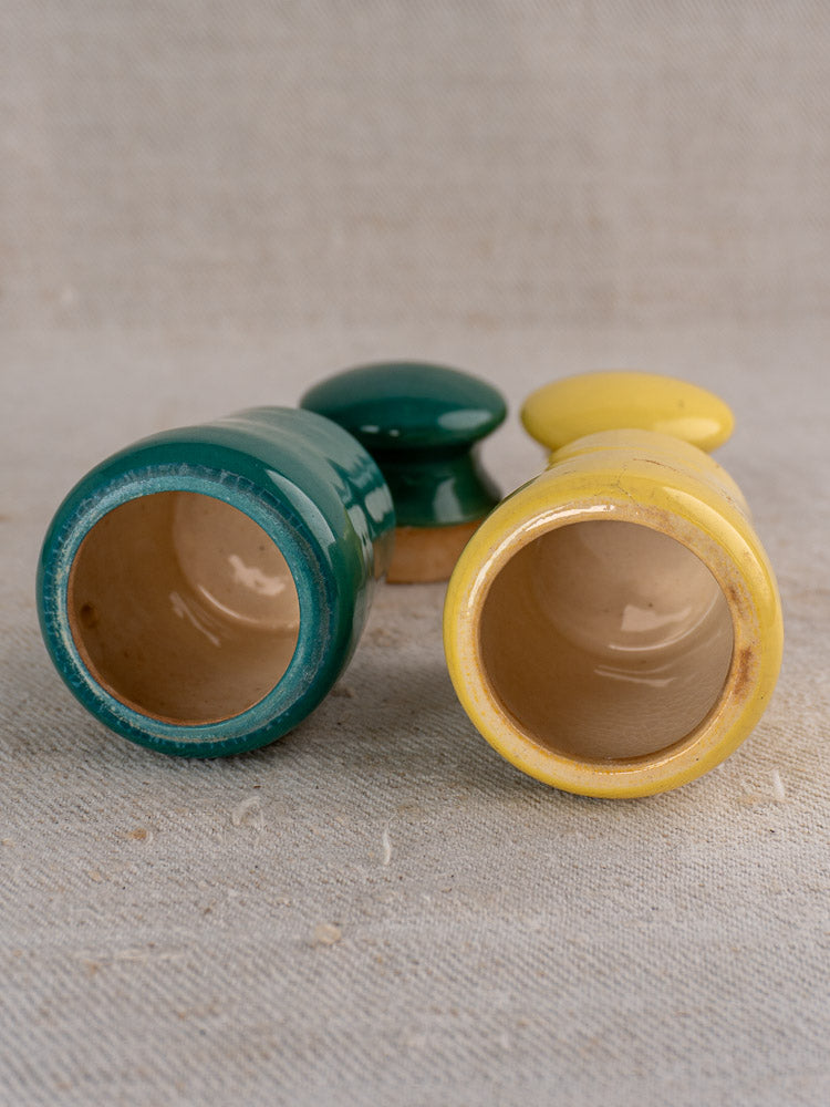 Pair of vintage French Maille mustard pots, teal and yellow, displayed on textured beige surface.