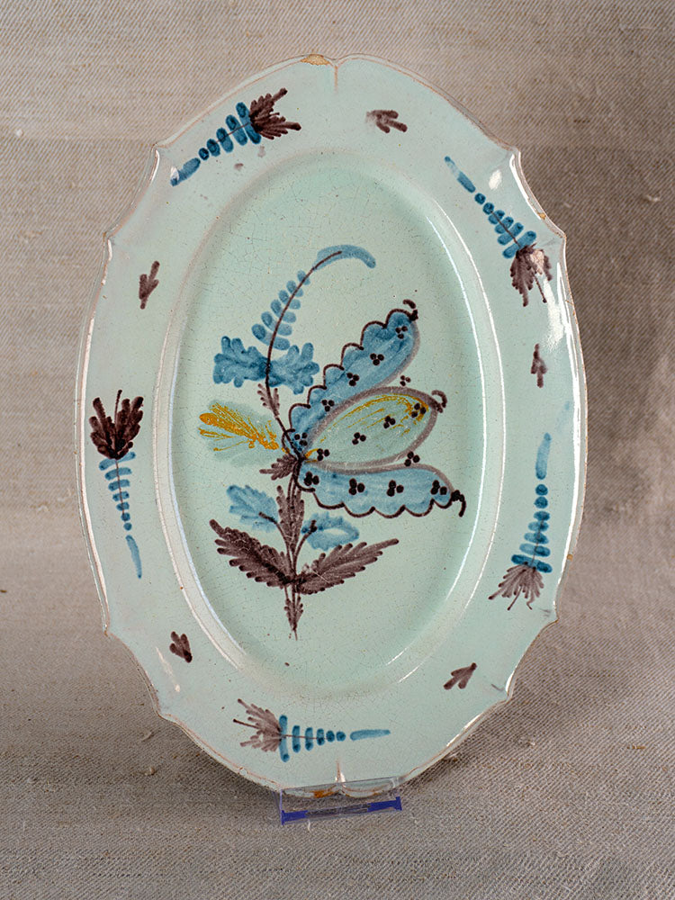 Antique French cul noir faience platter with scalloped edges, blue and brown butterfly and floral motifs, on light green.