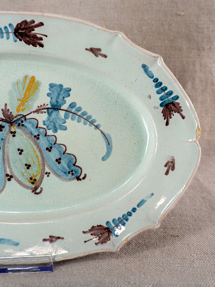 Antique French faience Cul Noir platter with light blue glaze, hand-painted floral motif, scalloped edge shows minor wear.