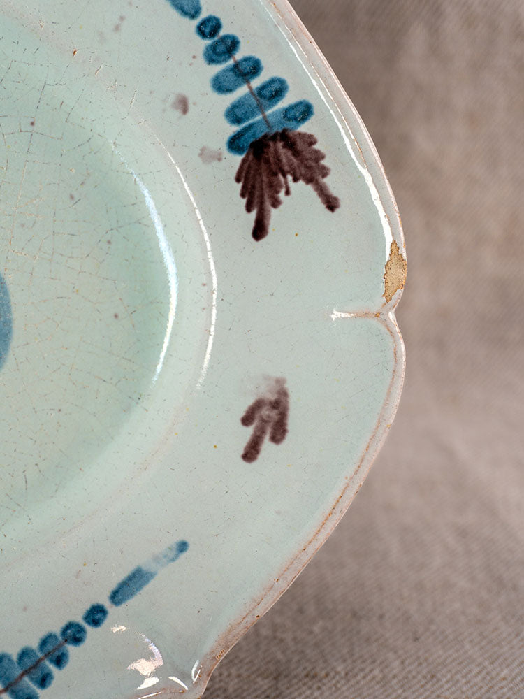 Antique French Cul Noir faience platter with chipped pale blue glaze and brown-blue rim, on textured beige surface.