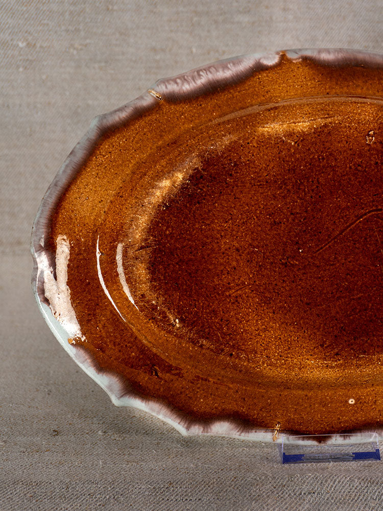 Antique French Cul Noir faience platter with glossy glaze and irregular white edges on neutral linen fabric.