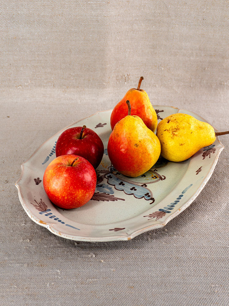 Antique French Cul Noir faience platter with three red apples and two yellow pears on textured beige fabric.