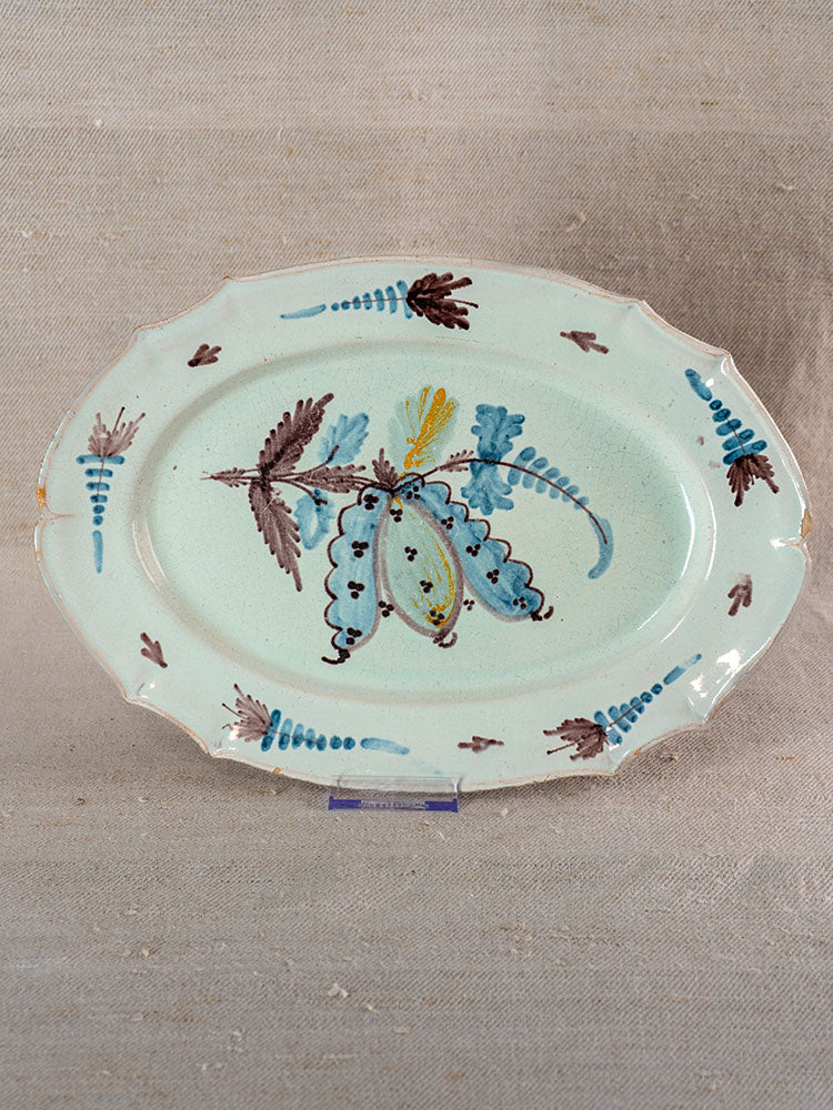 Antique French Cul Noir faience platter with scalloped edge and hand-painted floral motifs, shown on neutral fabric backdrop.
