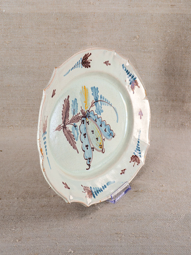 Antique French Cul Noir faience platter with scalloped edges, floral motifs, displayed upright on beige fabric.
