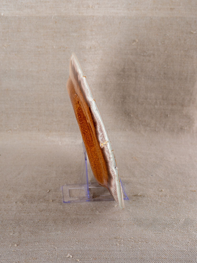 Antique French faience Cul Noir platter with earthy brown ceramic surface on clear stand, textured fabric backdrop.
