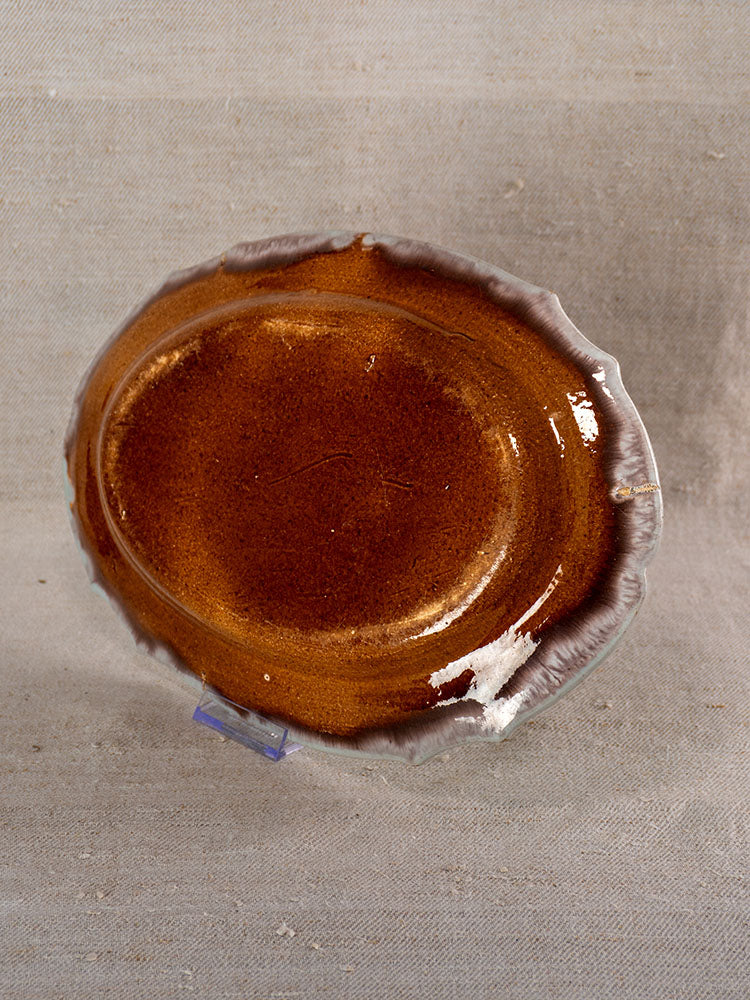 Antique French Cul Noir faience platter with brown glazed center and wavy grayish-white rim, set against beige fabric.