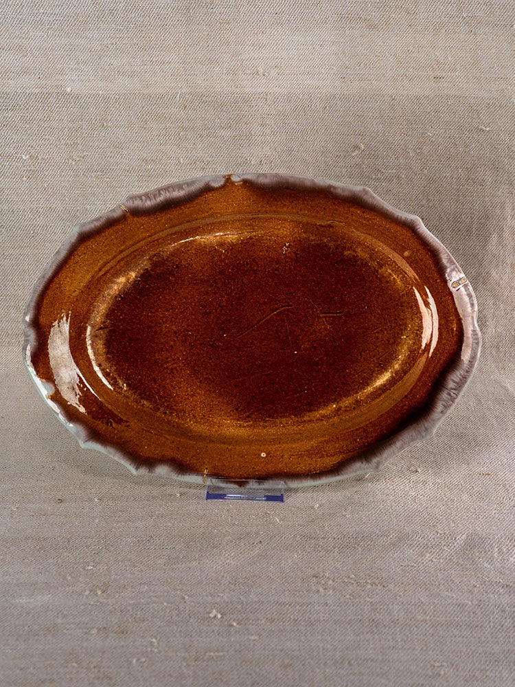 Antique French Cul Noir faience platter with glossy brown center, wavy rim, and pale gray edge against beige fabric.