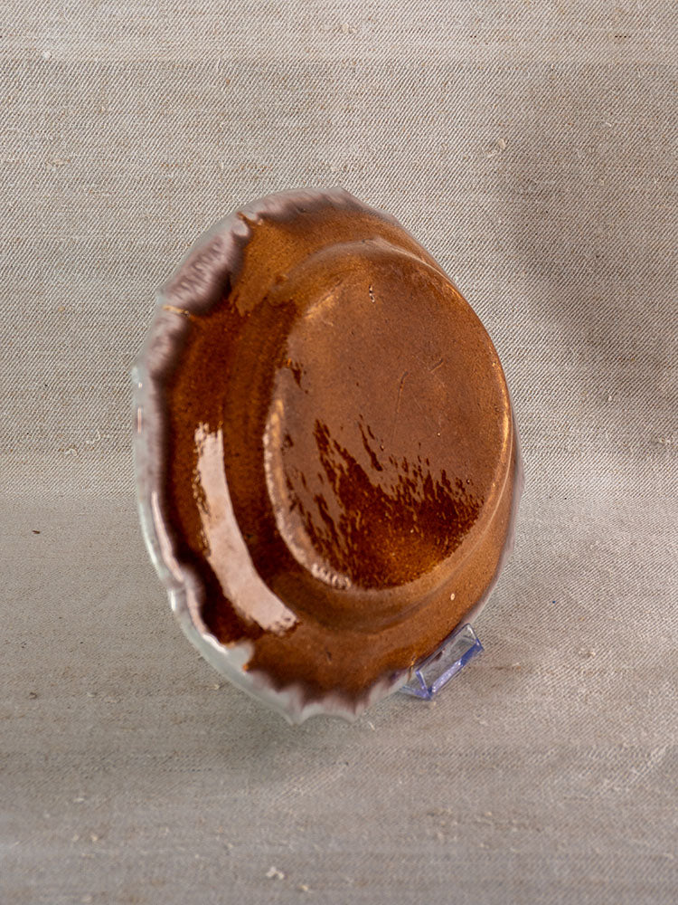 Late 18th-century French Cul Noir faience platter with glossy brown glaze, uneven rim on textured neutral fabric.