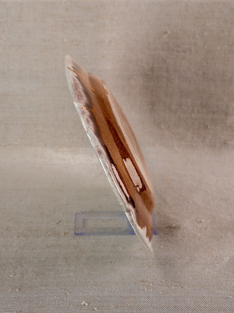 Antique French Cul Noir faience platter with brown and beige marbled design on clear stand, textured beige backdrop.
