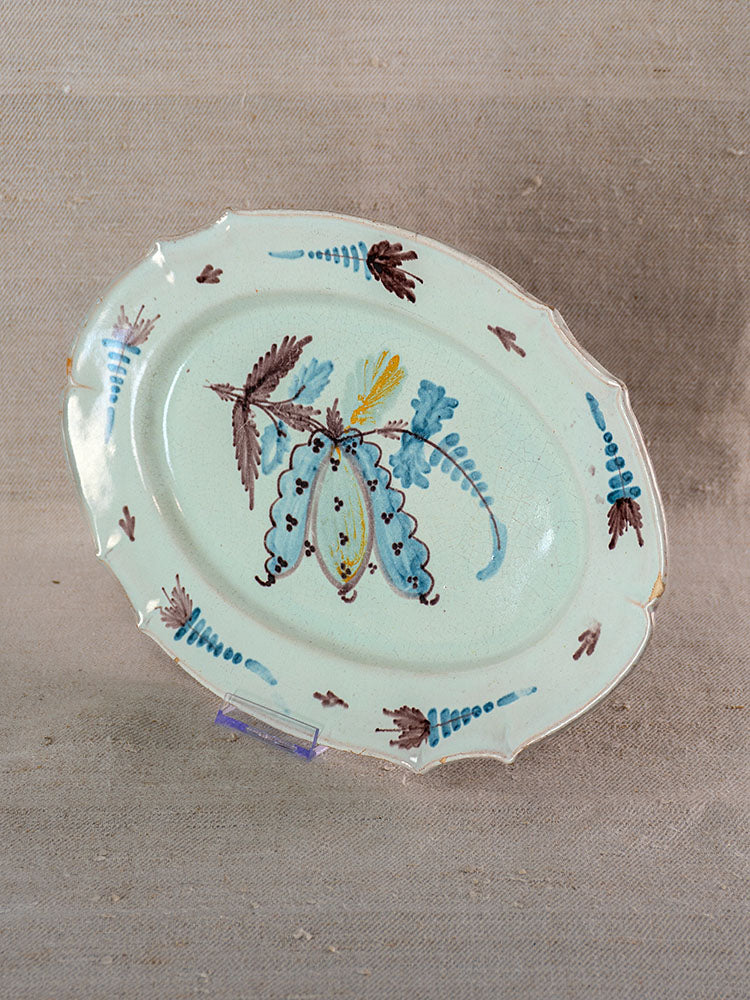 Late 18th-century French Cul Noir faience platter, oval with blue glaze, floral details, scalloped edge, on fabric backdrop.