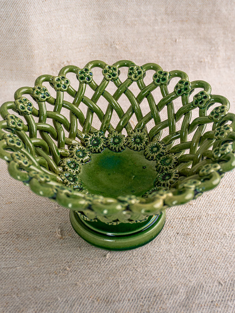 Vintage French Pichon Uzès basket with green glaze and open lattice design on beige textured fabric.