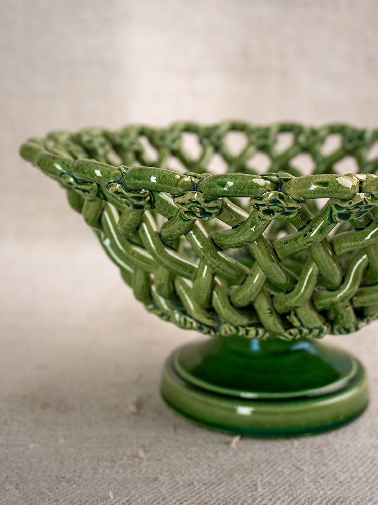 Vintage French Pichon Uzès green glazed woven basket with lattice design and pedestal base on beige textured fabric background.