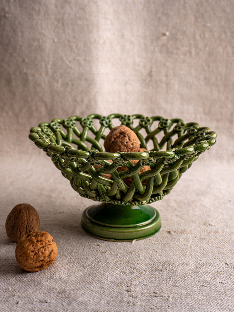 Mid-century French Pichon Uzès woven basket with green glaze, holding walnuts on textured beige fabric.