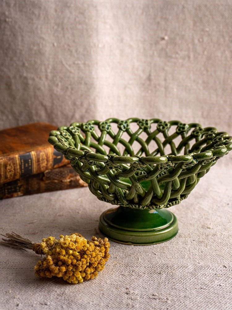Vintage French Pichon Uzès woven basket with green glaze on textured cloth, beside dried yellow flowers and an old brown book.