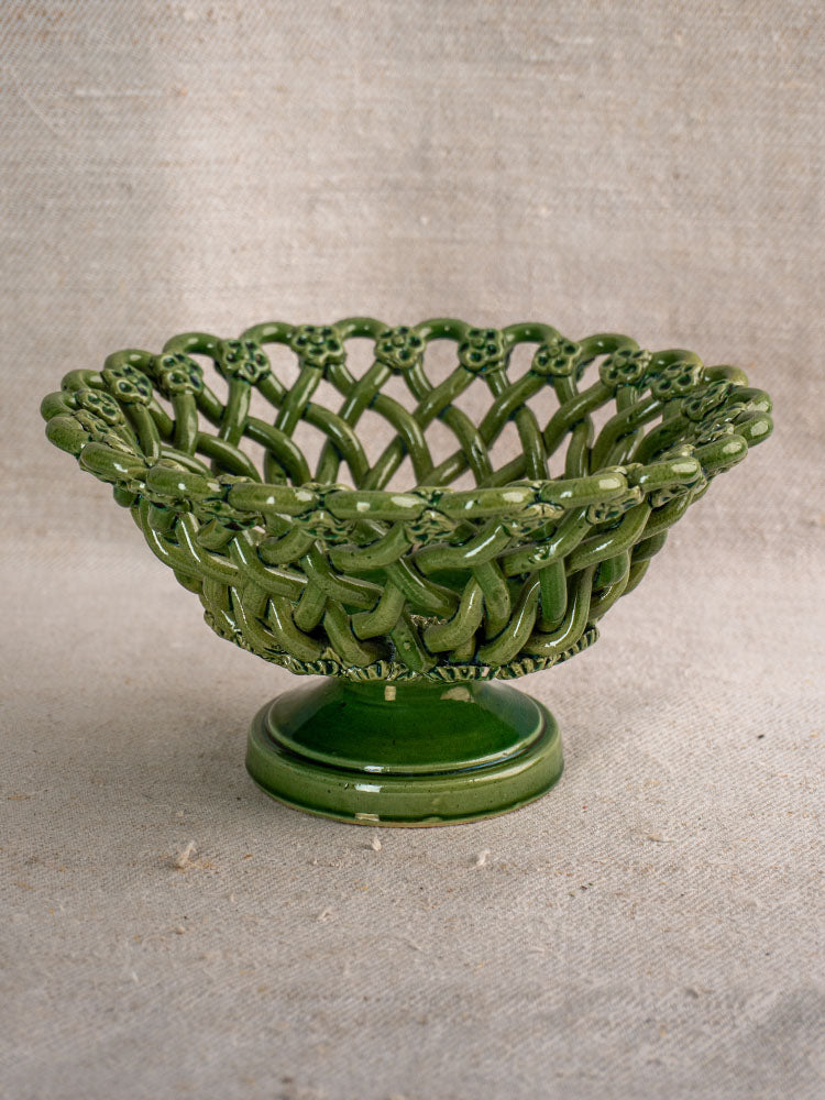 Vintage French Pichon Uzès woven basket with green glaze and open-weave design on pedestal base, set against beige fabric.