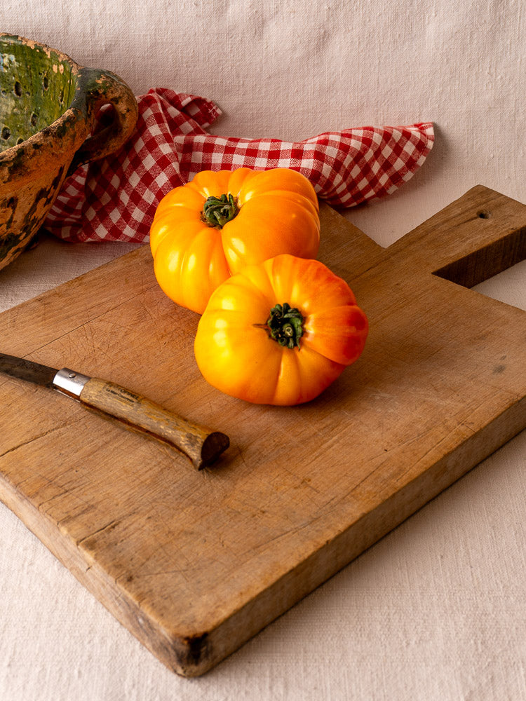 Antique French hardwood Provencal cutting board with yellow heirloom tomatoes and wooden-handled knife; rustic bowl behind.
