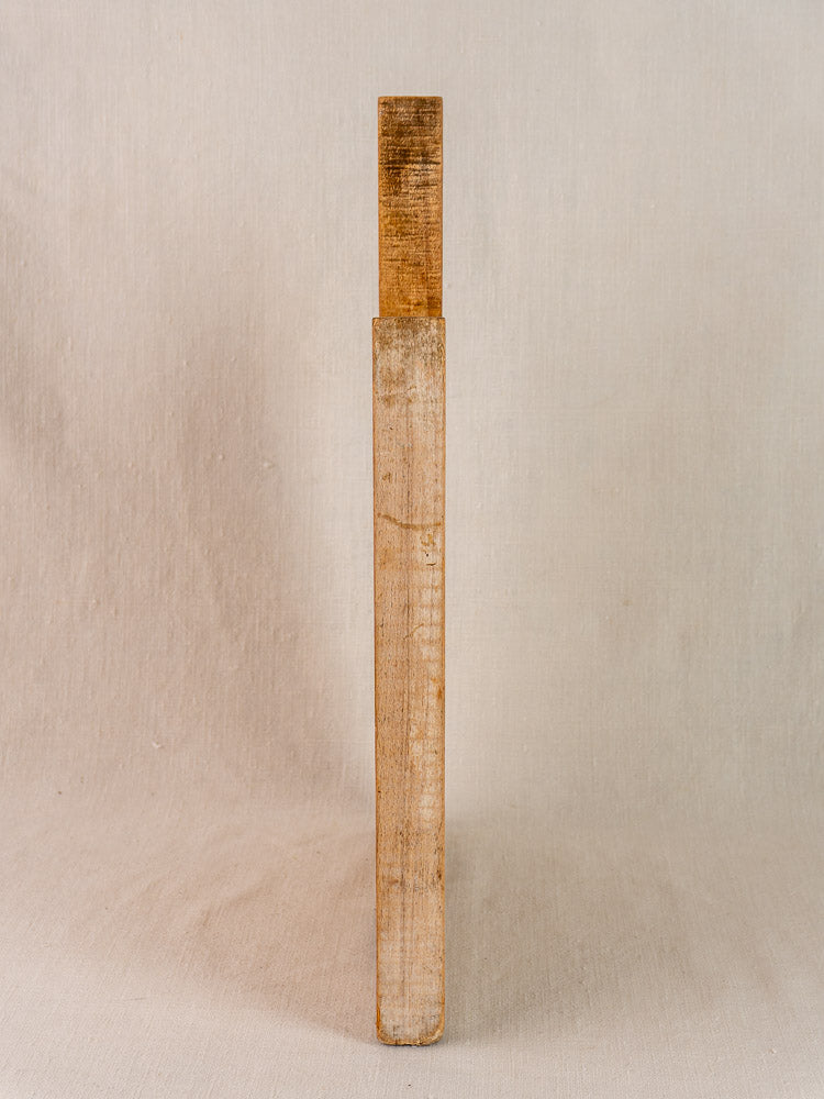Antique French hardwood cutting board in traditional Provencal style, upright on textured surface, beige background.