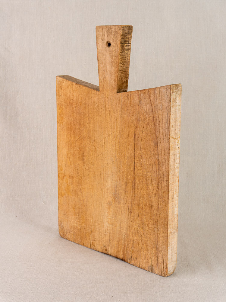 Antique French Provencal hardwood cutting board with short wide handle and hanging hole, displayed upright on a light background.