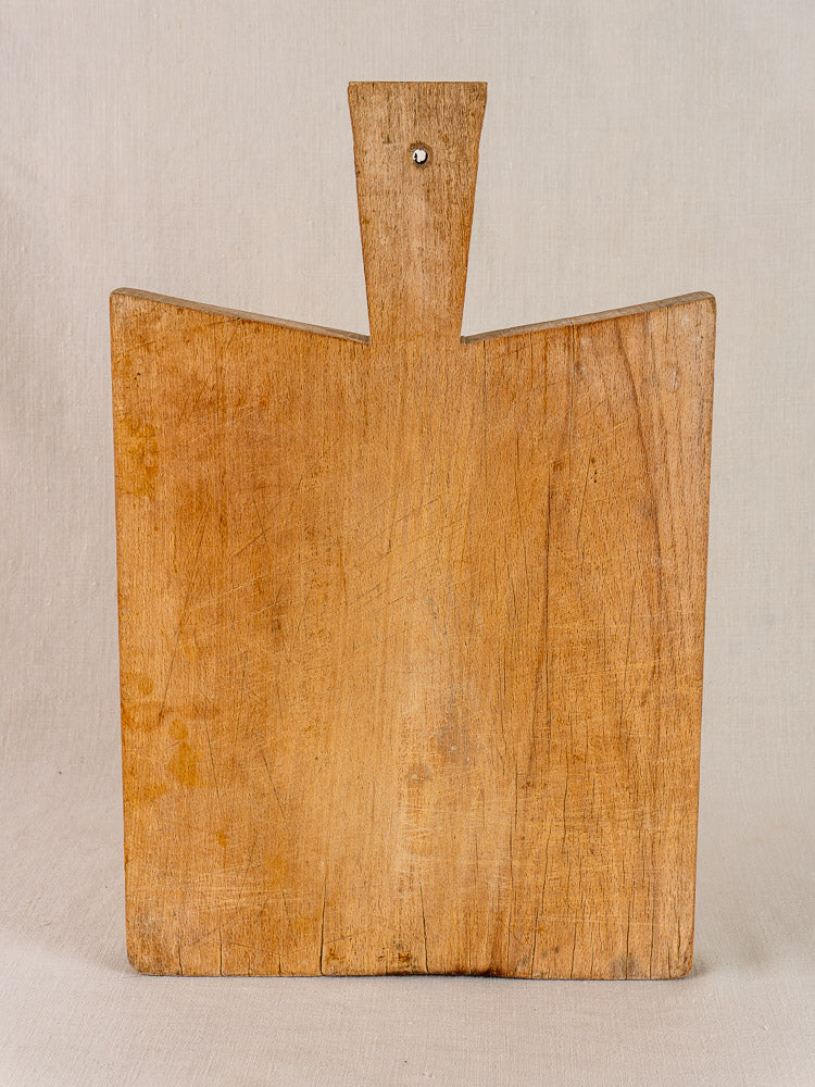 Antique French Provencal hardwood cutting board with short handle and visible grain, displayed upright for decor.
