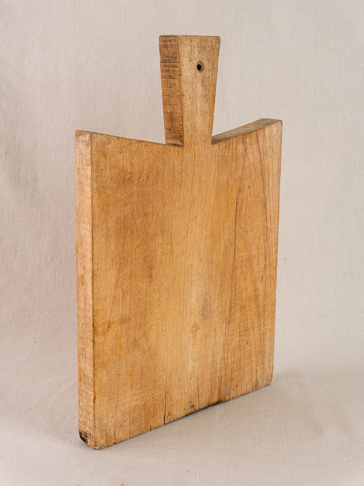 Antique French Provencal hardwood cutting board with short handle and visible grain, displayed on neutral fabric background.