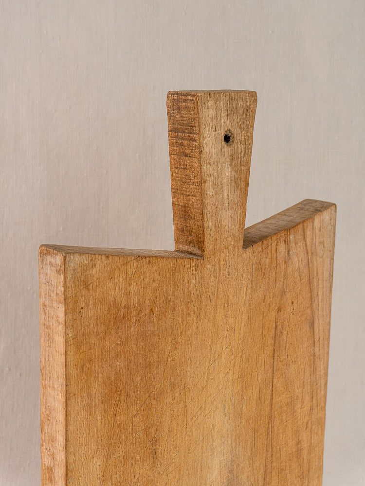 Antique French hardwood cutting board with rectangular shape and angular handle, natural finish, neutral backdrop.