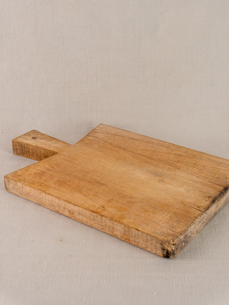Antique French hardwood cutting board with a rectangular shape, short handle, visible grain, and worn patina.