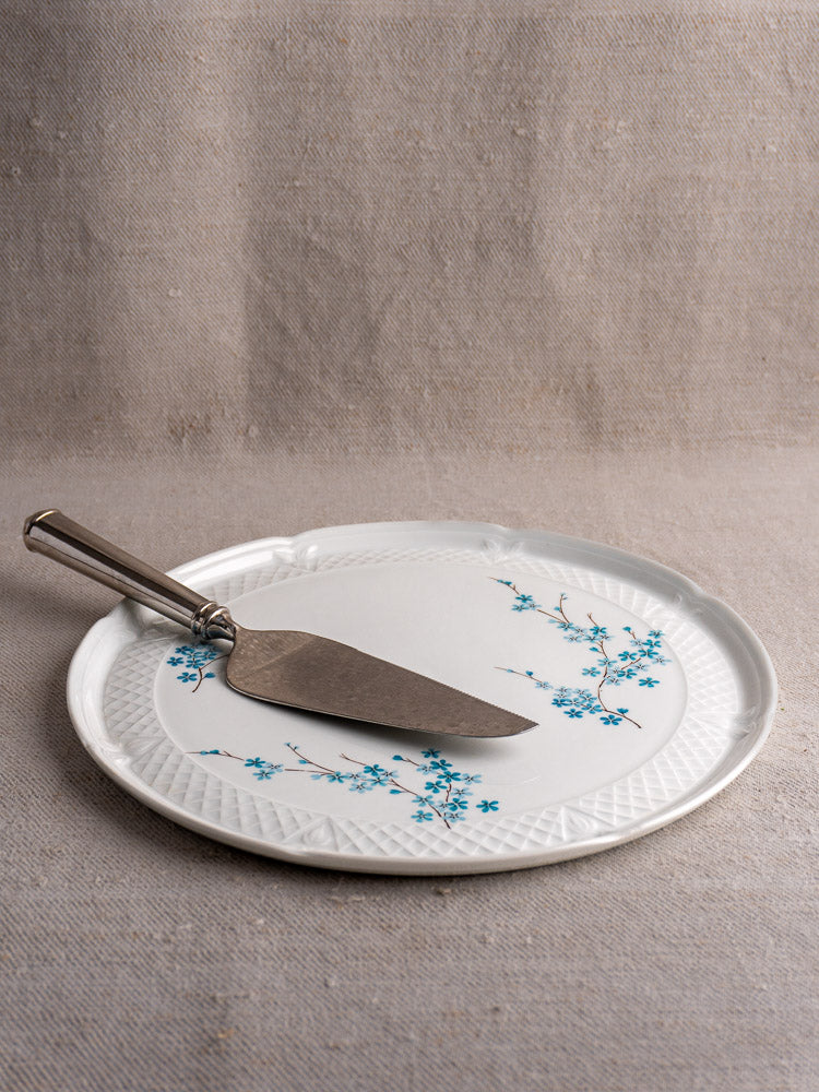 Berry Limoges Porcelain cake plate with blue floral design on white ceramic, displayed with metal pie server on beige surface.