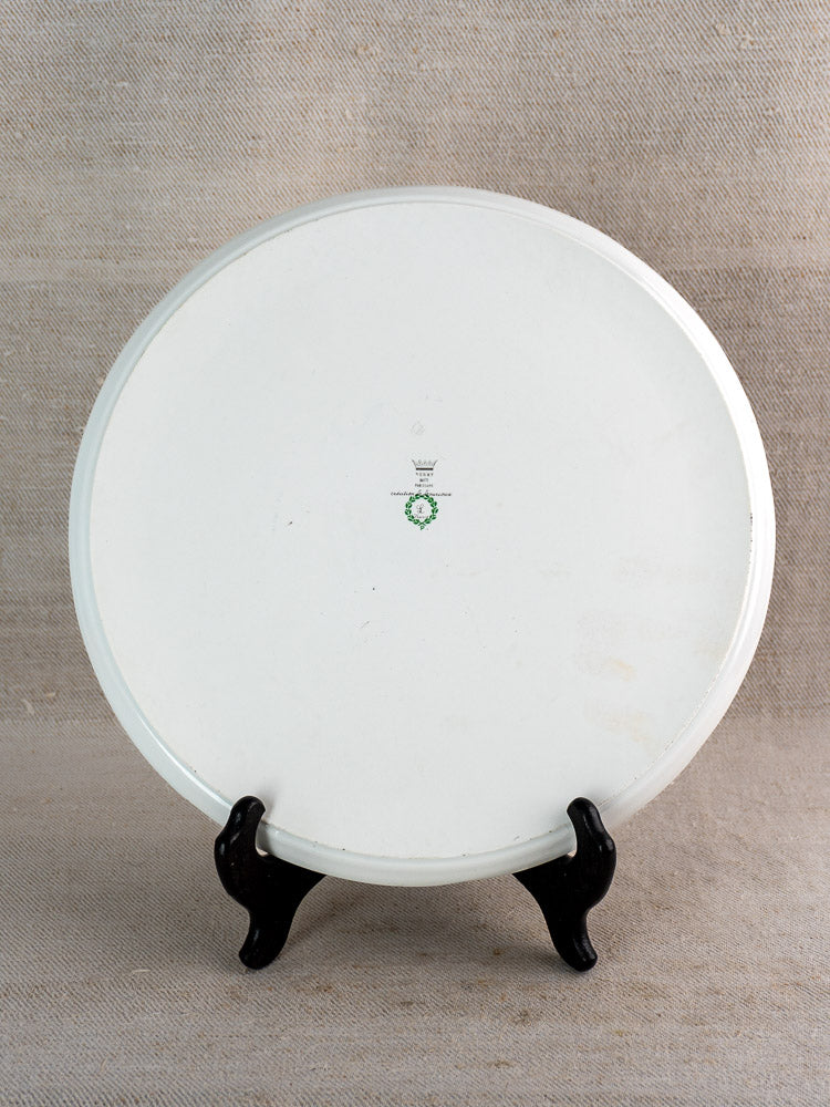 Vintage French Limoges porcelain cake plate on black stand, back view with green and black maker’s mark, beige textured backdrop.