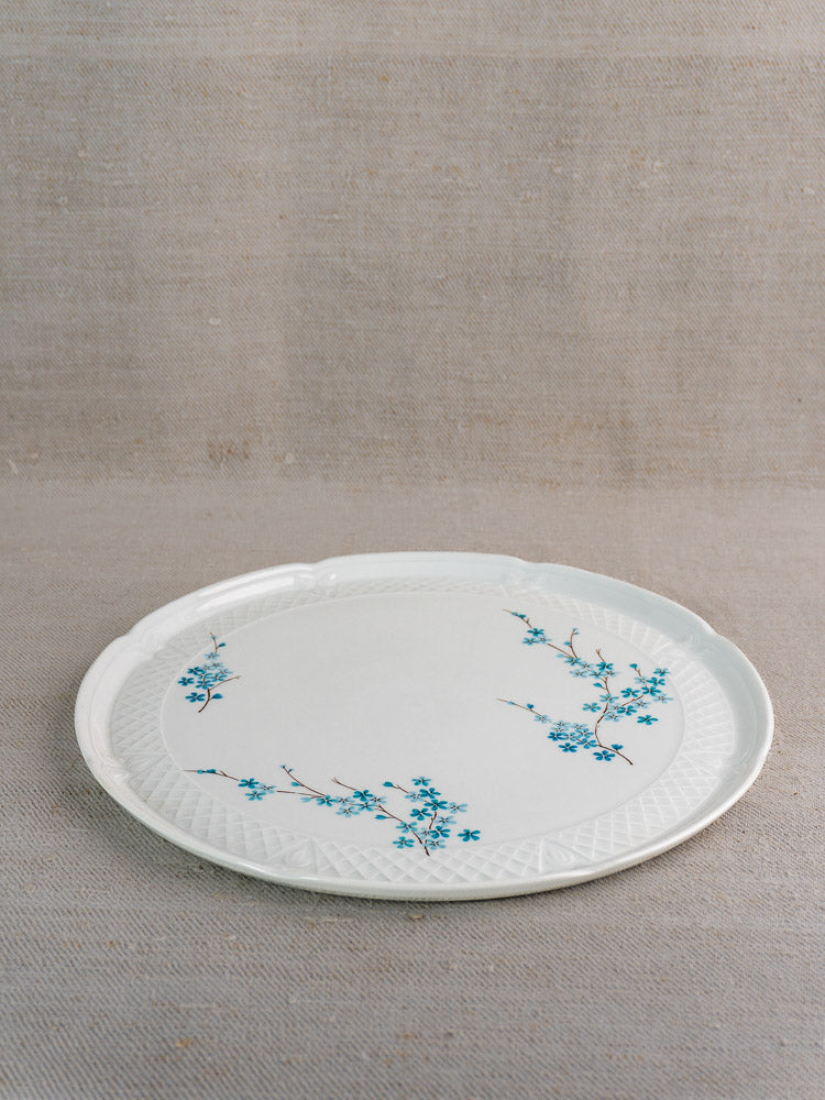 Berry Limoges vintage French cake plate with textured rim and blue floral pattern on beige fabric surface.