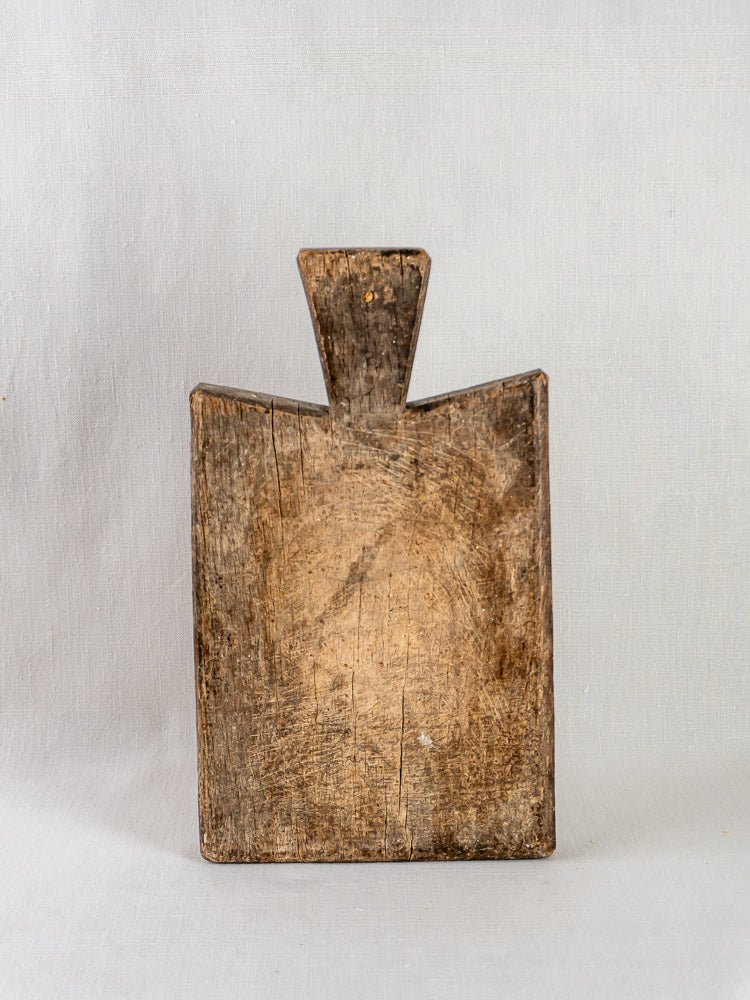 Antique French hardwood cutting board with triangular handle, upright on a light gray background.