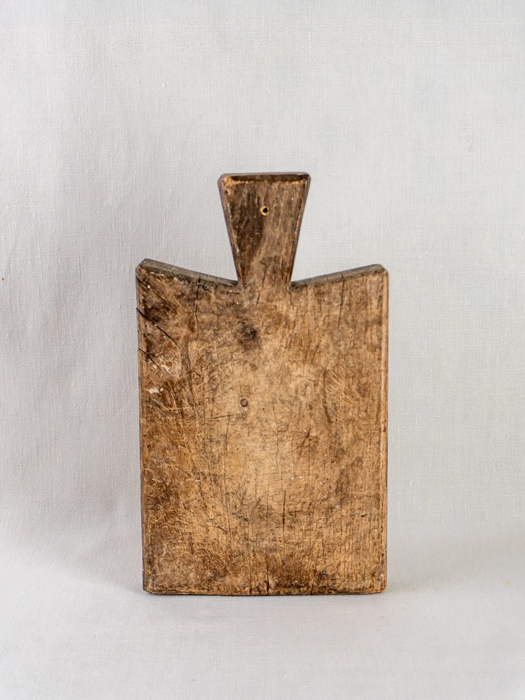 Antique 19th-century French hardwood cutting board with triangular handle, upright on light gray background.