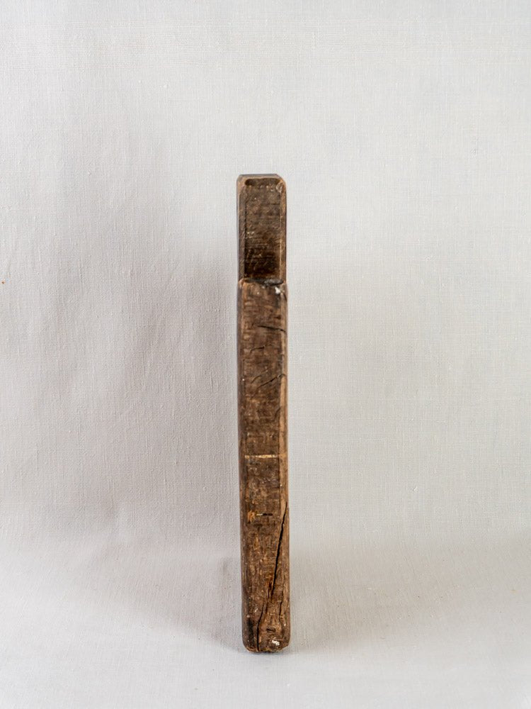 Antique 19th-century French hardwood cutting board with aged scratches, cracks, and worn edges upright on light fabric.