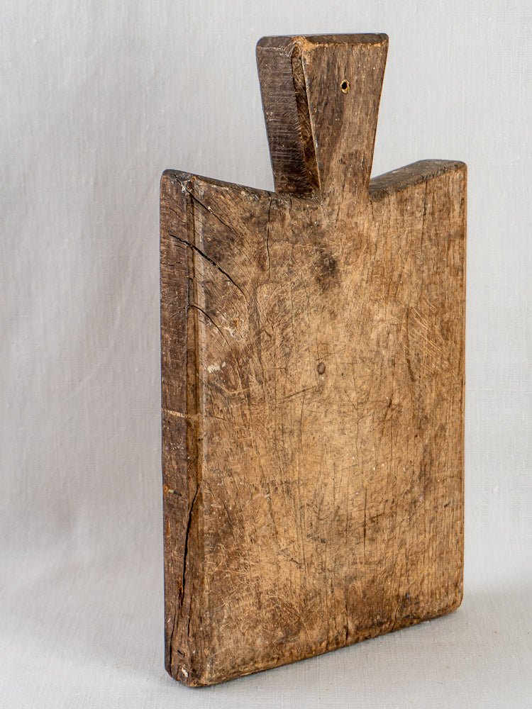Antique 19th-century French hardwood cutting board with short handle, upright on light gray surface.