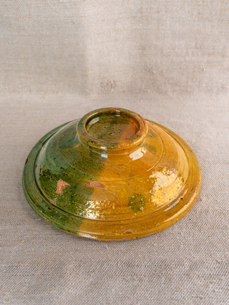Late 19th-century French Provençal compotier with green and ochre glaze, upside down on textured beige fabric.