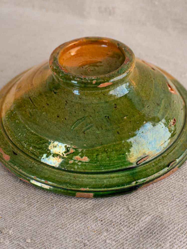 Antique French Provençal compotier with green and ochre glazed lid, circular handle, subtle chips on textured beige fabric.